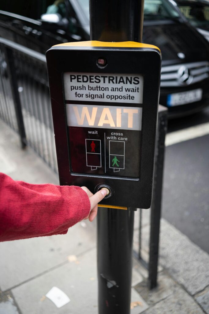 Person pressing pedestrian crossing button at street intersection in urban environment.